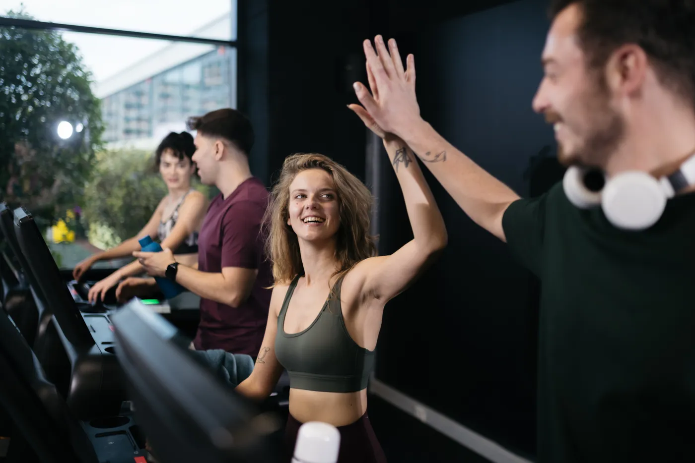 A coach high-fiving a client while two others train on treadmills beside her